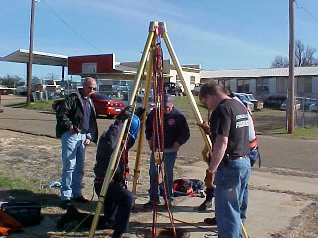 Fire fighters stand around the rigging designed to get them down the manhole.